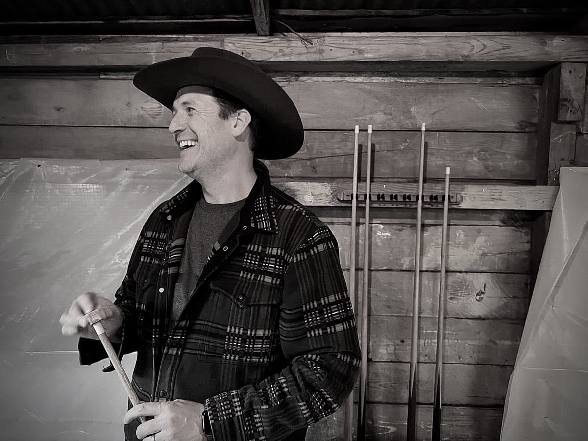 Casey Templeton in a cowboy hat and plaid jacket, laughing, photographed in black and white inside a wood-paneled room.